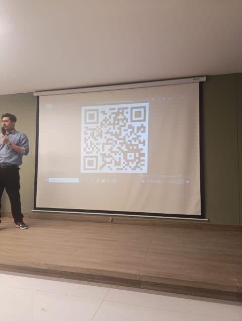Muzammil presenting at an Algorand event, a QR code on the screen behind him.